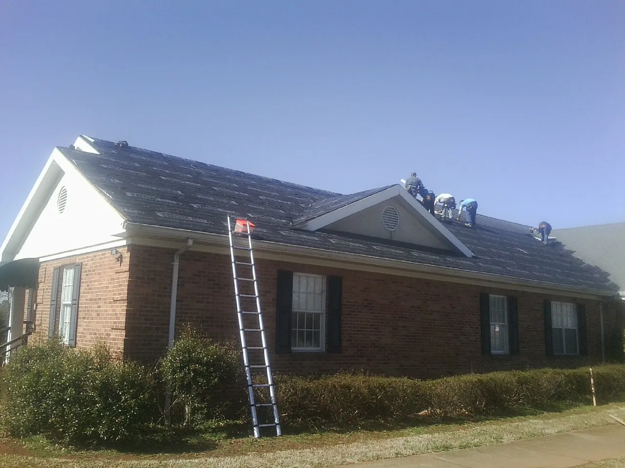 Crew tearing shingles off a brick ranch roof with a ladder set — Metal Roof Repair work by our crew in Pageland
