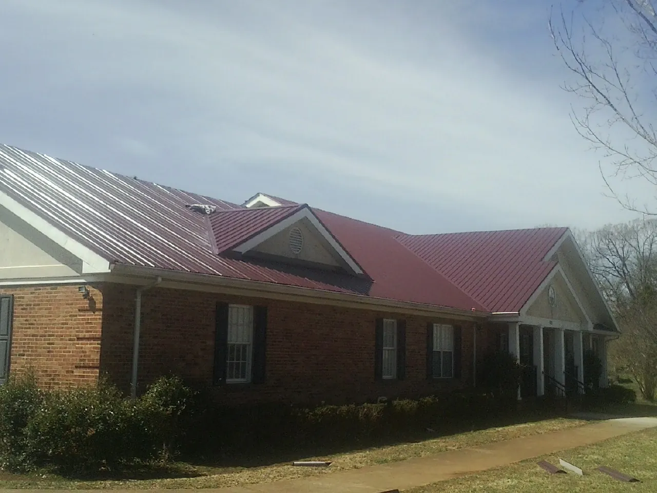 Red metal roof with gabled entries on a long brick building, from a Hail Damage Roof Repair job in Pageland