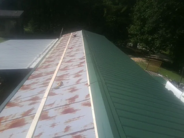 Old rusted panels beside newly installed green metal roofing — Wind Damage Roof Repair by Roofing Brothers in Pageland