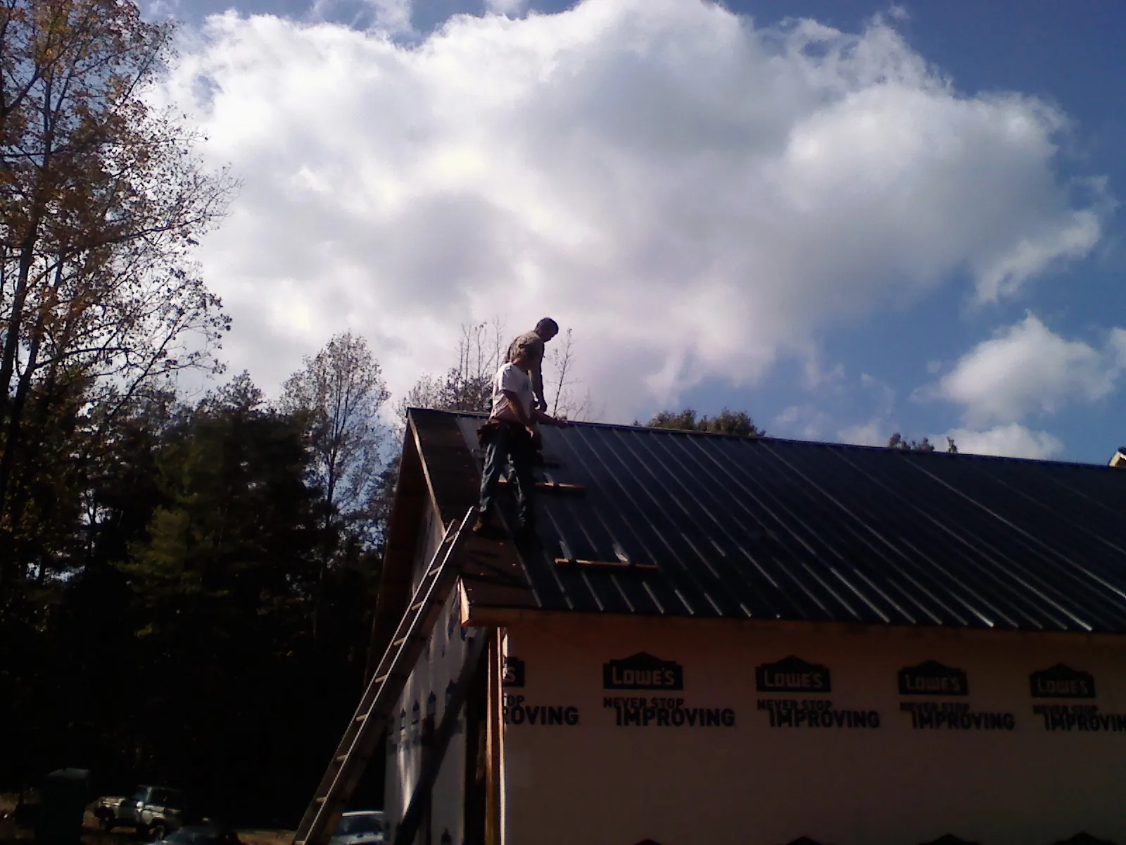 Roofer fastening dark metal panels high against a cloudy sky, from a Roof Inspection job in Pageland