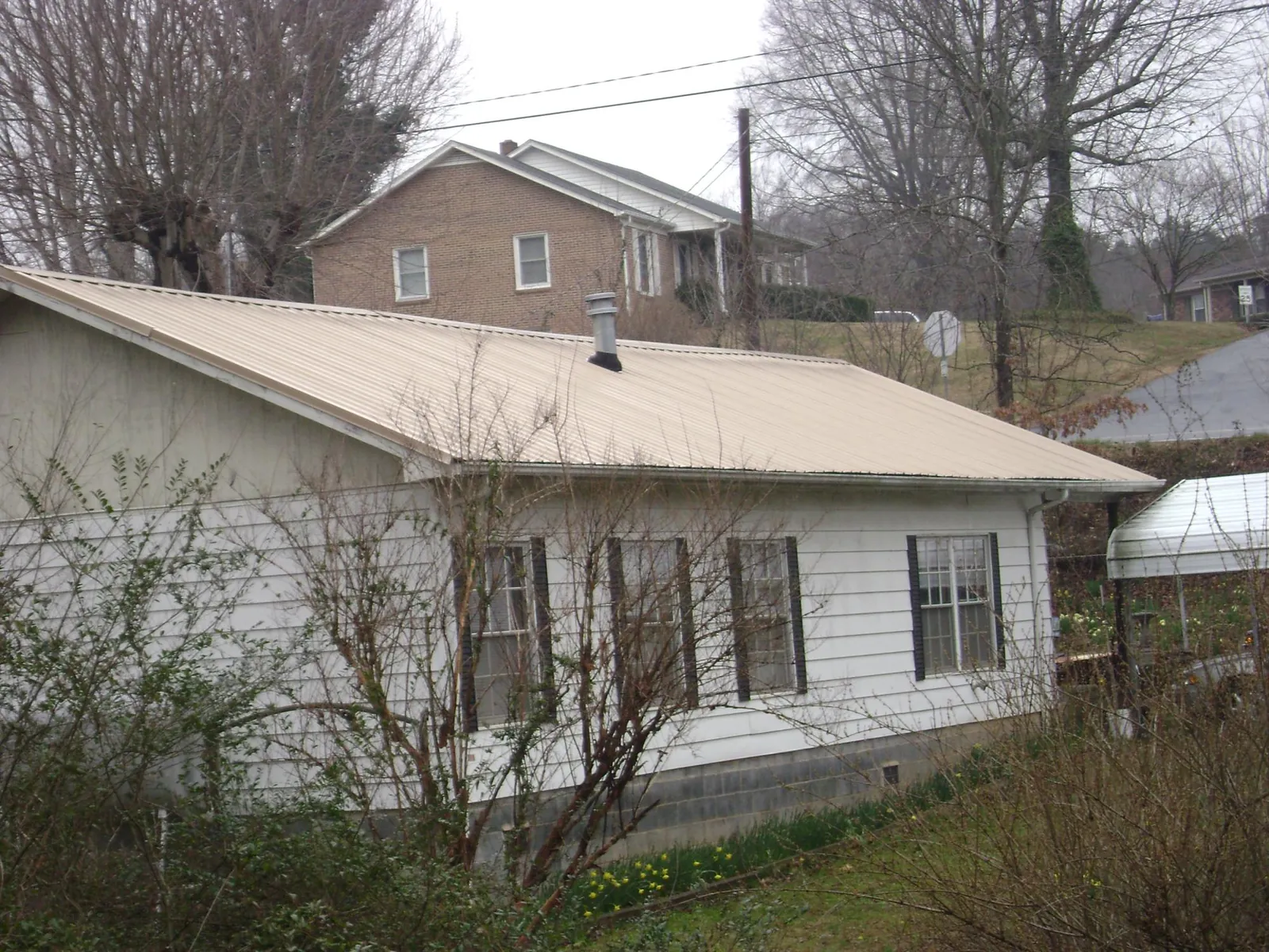 Tan metal roof on a white sided house set into a hillside — Commercial Roofing by Roofing Brothers in Pageland